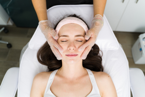 Verjongende behandeling. Vrouwelijke jonge klant hydrateert haar huid met een gezichtsbehandeling in de beauty clinic  - Foto, afbeelding