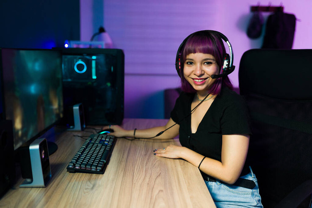 Attractive female gamer with a headset looking at the camera and smiling while taking a break from playing online videogames - Fotografie, Obrázek