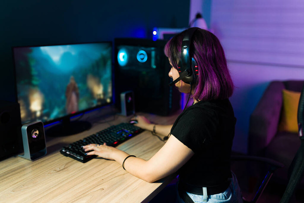 Achteraanzicht van een jonge latijnse vrouw zitten aan haar bureau en genieten van een online video game  - Foto, afbeelding