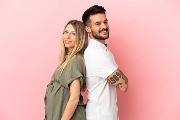 Pregnant woman and man over isolated pink background keeping arms crossed - Foto, imagen