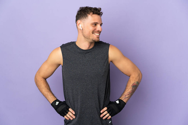 Young caucasian handsome man isolated on purple background posing with arms at hip and looking side - Photo, Image