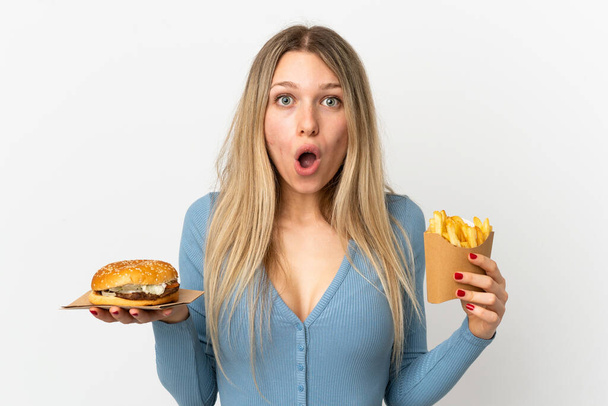 Nuori blondi nainen tilalla paistettuja sipsejä ja juustohampurilainen yli eristetty tausta - Valokuva, kuva