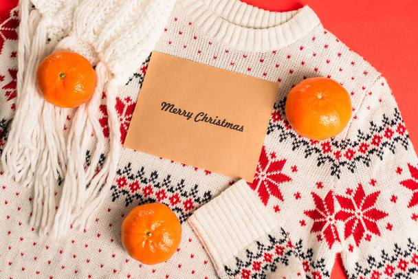 top view of greeting card with merry christmas lettering near tangerines on knitted sweater  - Photo, Image