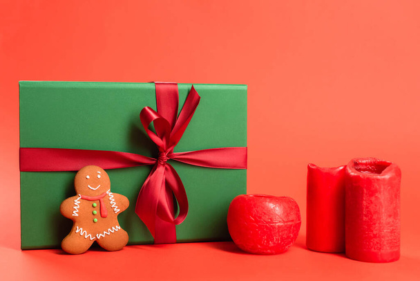 gingerbread cookie near green wrapped present and candles on red - Fotografie, Obrázek