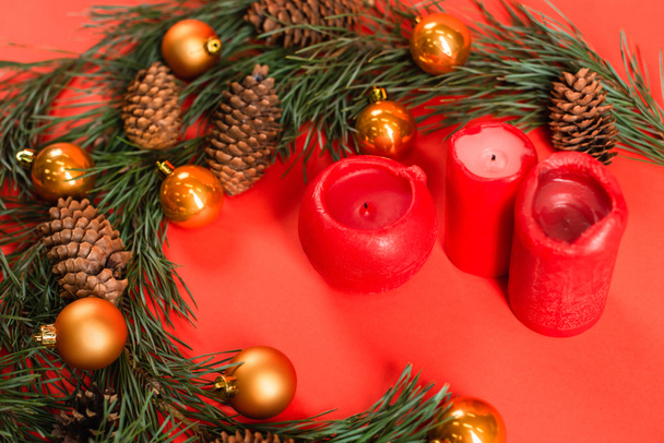 high angle view of pine cones near green branches with christmas balls and candles on red - Foto, Imagen