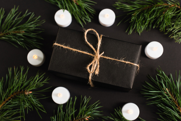 vista superior de la caja de regalo cerca de velas y ramas de pino en negro - Foto, imagen
