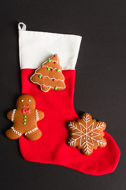 top view of different shapes gingerbread cookies on red christmas stocking isolated on black  - Photo, Image