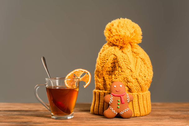 glass cup of tea with sliced orange near knitted hat and gingerbread cookie isolated on grey - Photo, Image