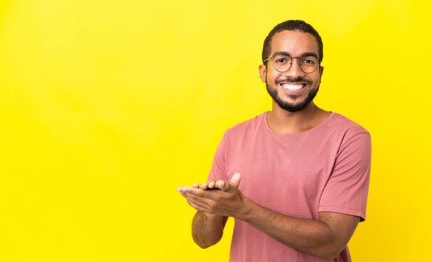 Junger lateinischer Mann auf gelbem Hintergrund applaudiert - Foto, Bild