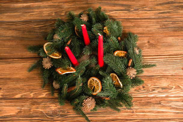 木製の表面に赤いキャンドルと緑のフィット枝とクリスマスリースのトップビュー - 写真・画像