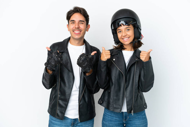 Jeune couple mixte avec un casque de moto isolé sur fond blanc donnant un geste pouce levé avec les deux mains et souriant - Photo, image