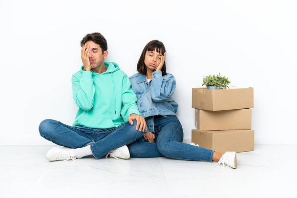 Junges Paar macht einen Schritt, während es eine Kiste voller Dinge aufhebt, die isoliert auf weißem Hintergrund auf dem Boden sitzen und überrascht und schockiert sind - Foto, Bild
