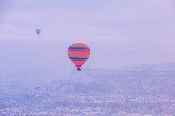 Hot air balloons flying over spectacular Cappadocia. Beautiful view of hot air balloons floating in sunrise blue sky over the mountain landscape of fairy chimneys - Foto, imagen