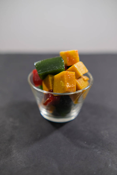 Ποτήρι από πολύχρωμες φέτες πάστας φρούτων Μεξικού σε μαύρη επιφάνεια - Φωτογραφία, εικόνα
