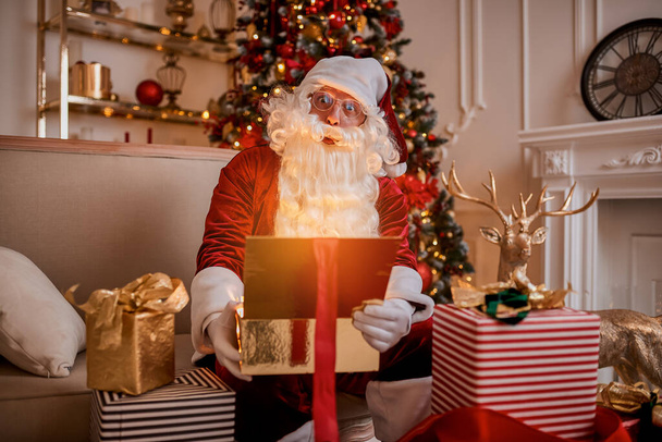 Surprised Santa Claus with a magical glowing gift near beautiful christmas tree.  New year and Merry Christmas , happy holidays concept - Фото, изображение