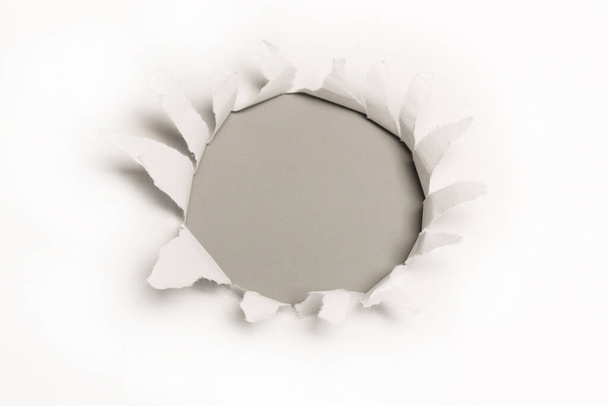 A hole in a white paper on a grey background, copy space.  - Photo, Image