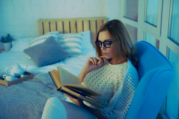 Free time. Girl reading book, sitting in armchair against window - Zdjęcie, obraz