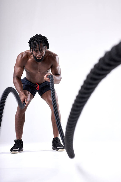 Athlete young african american man doing cross fit exercises with ropes - Фото, изображение