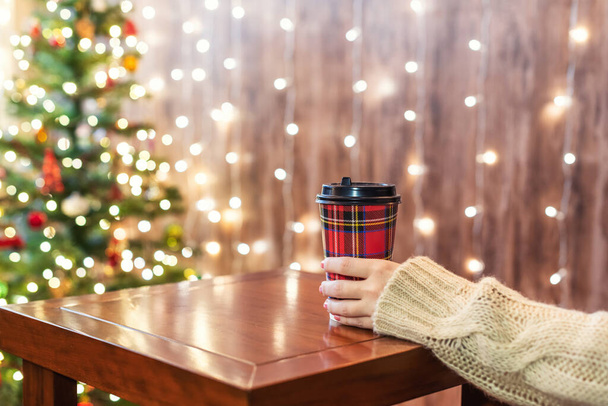Woman drinking hot chocolate in paper cup on the background of Christmas tree - Фото, зображення