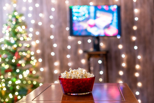 Red bowl with popcorn on the background of TV and Christmas tree  - Фото, зображення