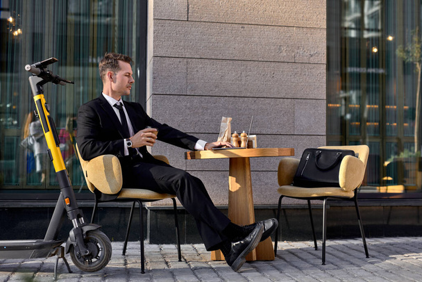 caucasian guy in formal stylish suit sit in outdoor cafe working online using laptop - Fotoğraf, Görsel