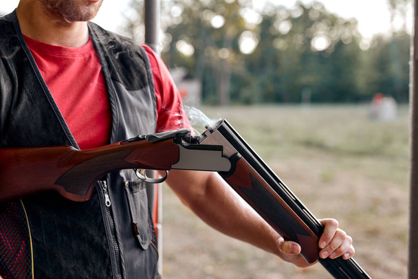 Cropped young man charges pump-action shotgun in an outdoor range. - Foto, Imagen