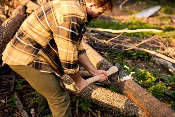 Γενειοφόρος ξυλοκόπος κόβει δέντρα με τσεκούρι. Άγριος γενειοφόρος ξυλοκόπος με τσεκούρι στο δάσος - Φωτογραφία, εικόνα