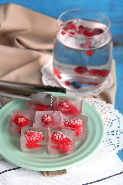 Ice cubes with raspberry on plate, on color wooden background - Fotó, kép