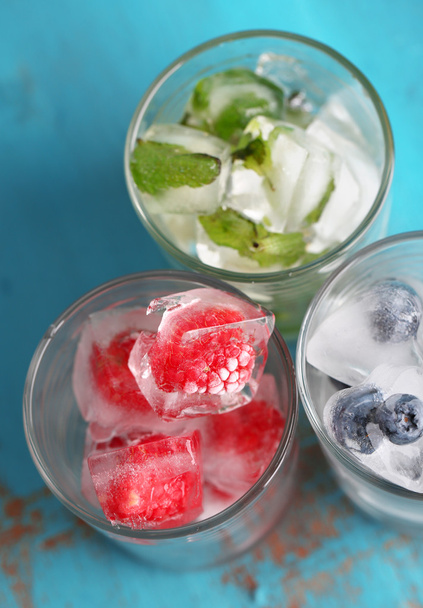 Ice cubes with mint leaves, raspberry and blueberry in glasses, on color wooden background - Foto, Bild