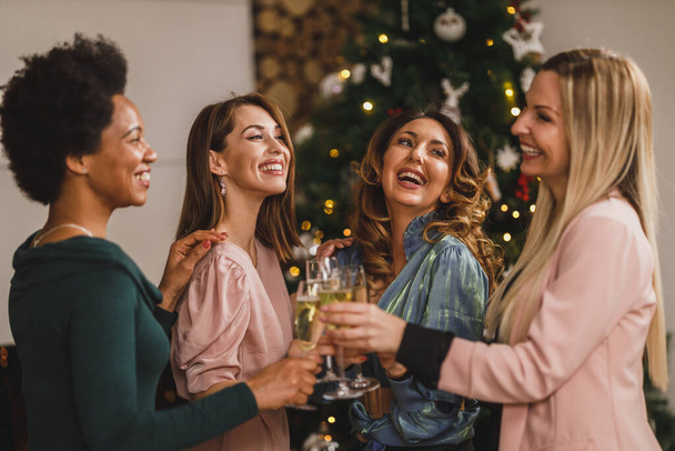 Веселые мультиэтнические девушки веселятся во время тоста с шампанским на Рождество или на новогодней вечеринке вместе. - Фото, изображение