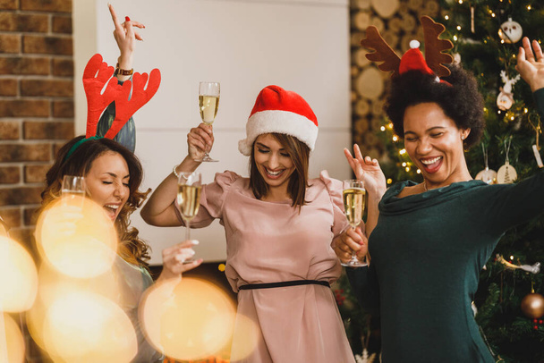 Vrolijke multietnische meisjes dansen en plezier hebben tijdens het toasten met champagne op nieuwjaarsfeest samen. - Foto, afbeelding