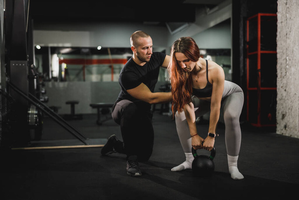 Aufnahme einer muskulösen jungen Frau, die mit Personal Trainer im Fitnessstudio trainiert. Sie macht Übungen mit der Kettlebell. - Foto, Bild