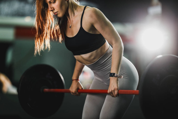 体育館でのハードトレーニングで働くスポーツウェアを着た筋肉質の若い女性のショット。彼女は重い重量で筋肉をポンプアップしています. - 写真・画像