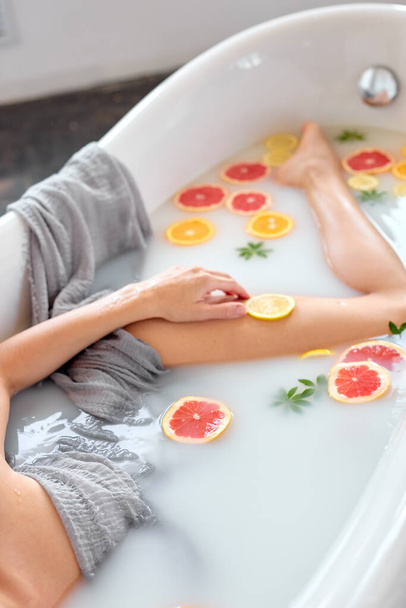 Unrecognizable slender woman enjoys bath with milk and juicy exotic fruits. body care. - 写真・画像