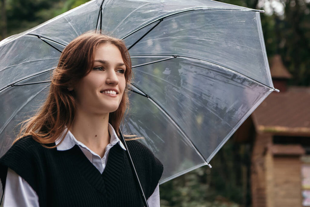 Femme tenir parapluie transparent à l'extérieur de la rue humide automne par temps nuageux parc pluvial. Dame se sentent protégés de l'eau goutte à goutte flaques d'eau. Espace de copie - Photo, image