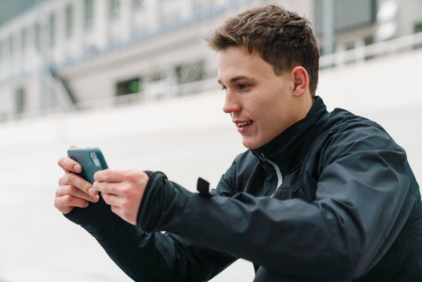 Vonzó fiatal sportoló mobiltelefont használ, miközben ül a stadionban, pihenés, játék - Fotó, kép