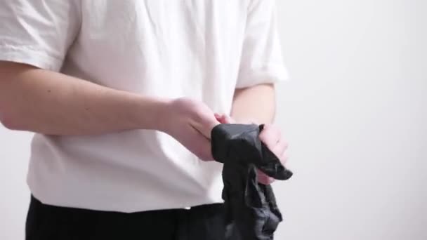 Un uomo in jeans neri e basica t-shirt bianca prende e indossa guanti neri - Filmati, video