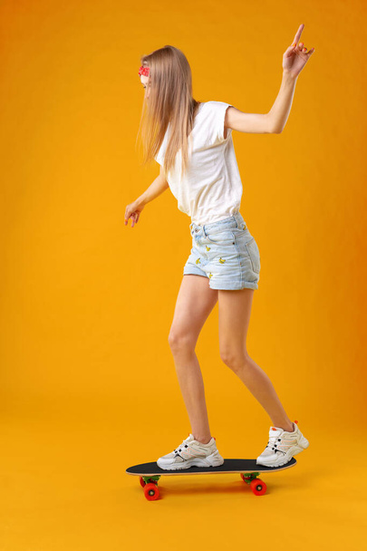 Teenager girl standing and posing on skateboard over a color background - Fotó, kép