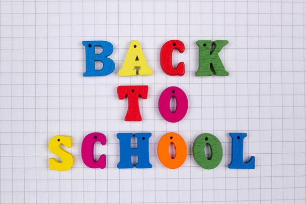 Inscription of the words of the slogan Back to school in multi-colored letters on a school squared notebook background. Colorful letters of the English alphabet. Education day. Spelling & orthography - Photo, image