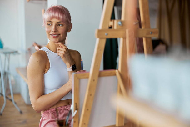 Elegant woman artist sits by easel with blank white canvas on at home - Photo, Image