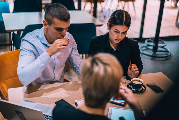 Κάτοψη ενός όμορφου νεαρού ζευγαριού που μιλάει στον μεσίτη του ενώ χρησιμοποιεί tablet και πίνει καφέ στο τραπέζι στο cafe - Φωτογραφία, εικόνα