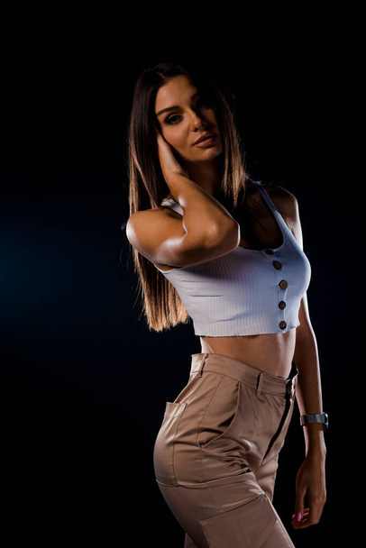 A young girl in a white jeans and sporty tank top on dark background - Foto, Imagem