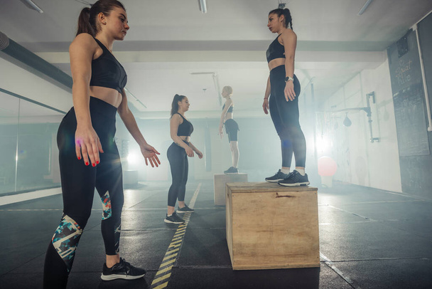 Adatta alle giovani donne che fanno esercizi di box squat nella palestra crossfit - Foto, immagini