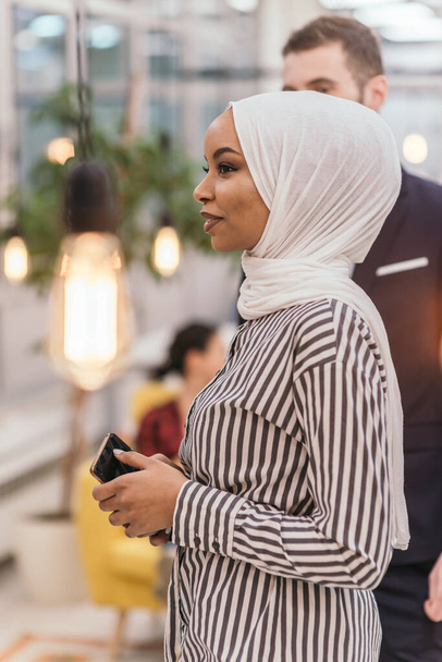 Портрет афро-американской мусульманки на работе, стоящей посреди современного офиса. - Фото, изображение
