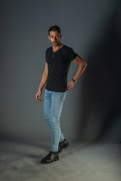 Студийная фотосессия красивого мужчины, позирующего в джинсах и черной рубашке - Фото, изображение
