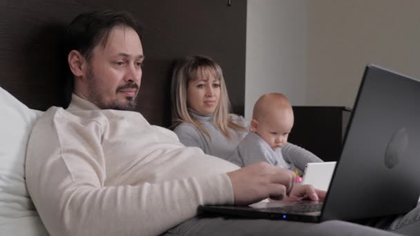 お父さんはコンピューターで自宅で働いているフリーランスで、お母さんは子供と遊んでいます。デジタルタブレットを持つコンピュータの子供の家で働いている子供を持つ家族。ホームオフィス、子供のための近代的な教育 - 映像、動画