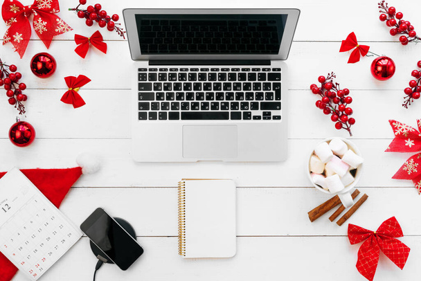 Laptop on white wooden desk surrounded with red Christmas decorations, top view - Foto, imagen