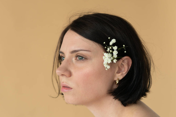 portrait of a young beautiful woman in profile, with a white flower behind her ear near a yellow wall - Foto, immagini