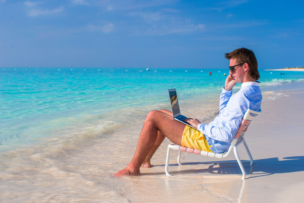 jonge man met laptop en mobiele telefoon op tropisch strand - Foto, afbeelding