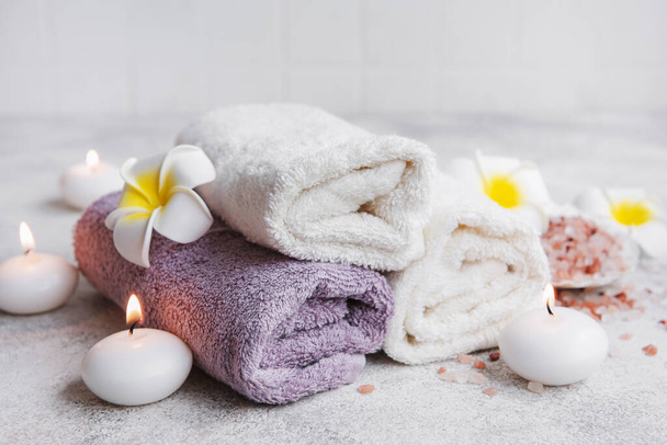 Ensemble spa, serviettes, sel de massage, bougie et fleurs frangipani sur fond de béton gris - Photo, image